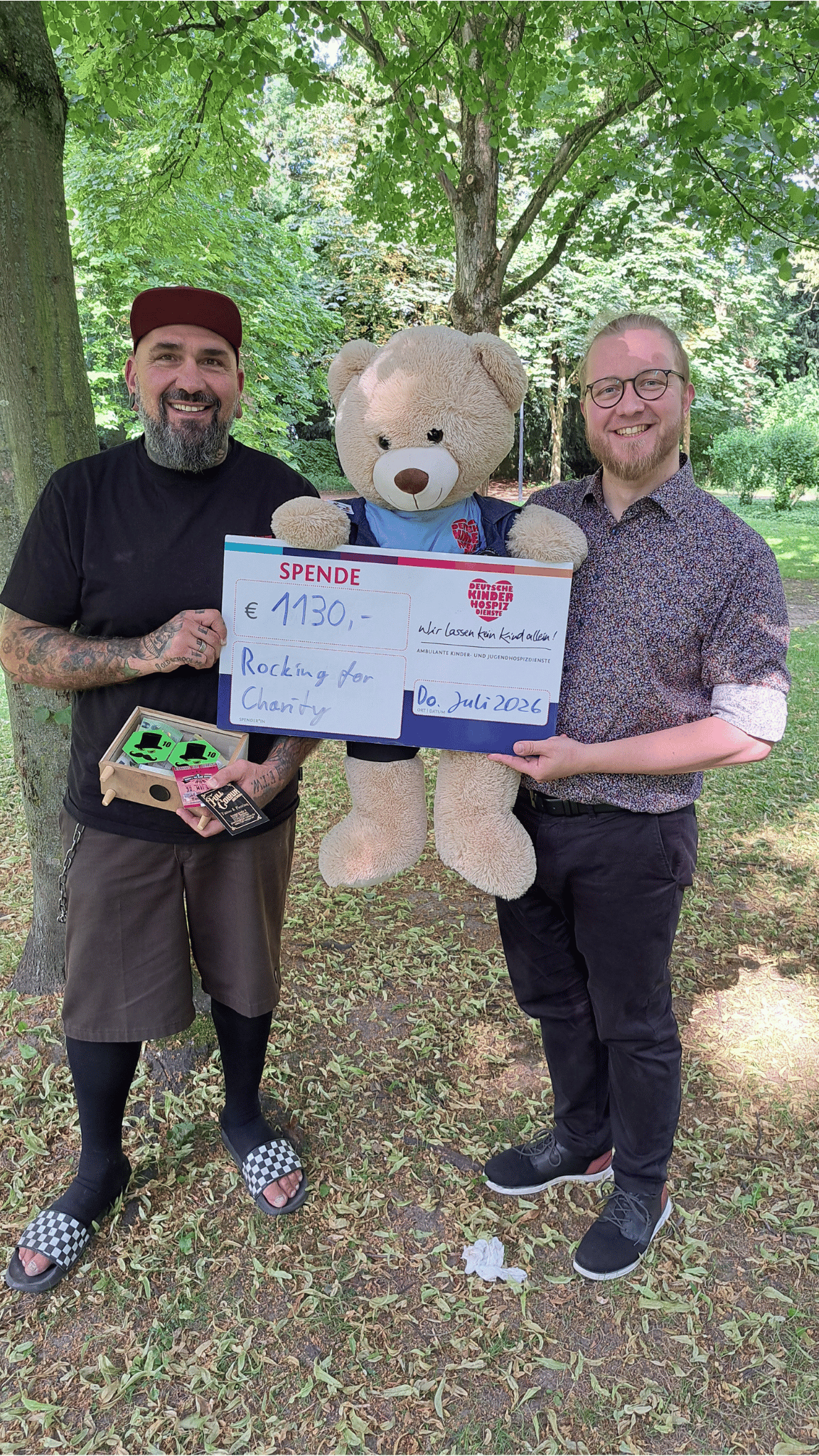 Obwohl das Event „Rocking for Charity“ Ende Mai kurzfristig abgesagt worden war, kamen 1130 Euro  zusammen, die Organisator Martin „Teddy“ Neumann (links) mit einem symbolischen Scheck an  Michael Cremann (rechts) und Bärenbotschafter Hope von den Deutschen Kinderhospiz Diensten  überreichte.  (Foto: Deutsche Kinderhospiz Dienste / Simke Strobler) 