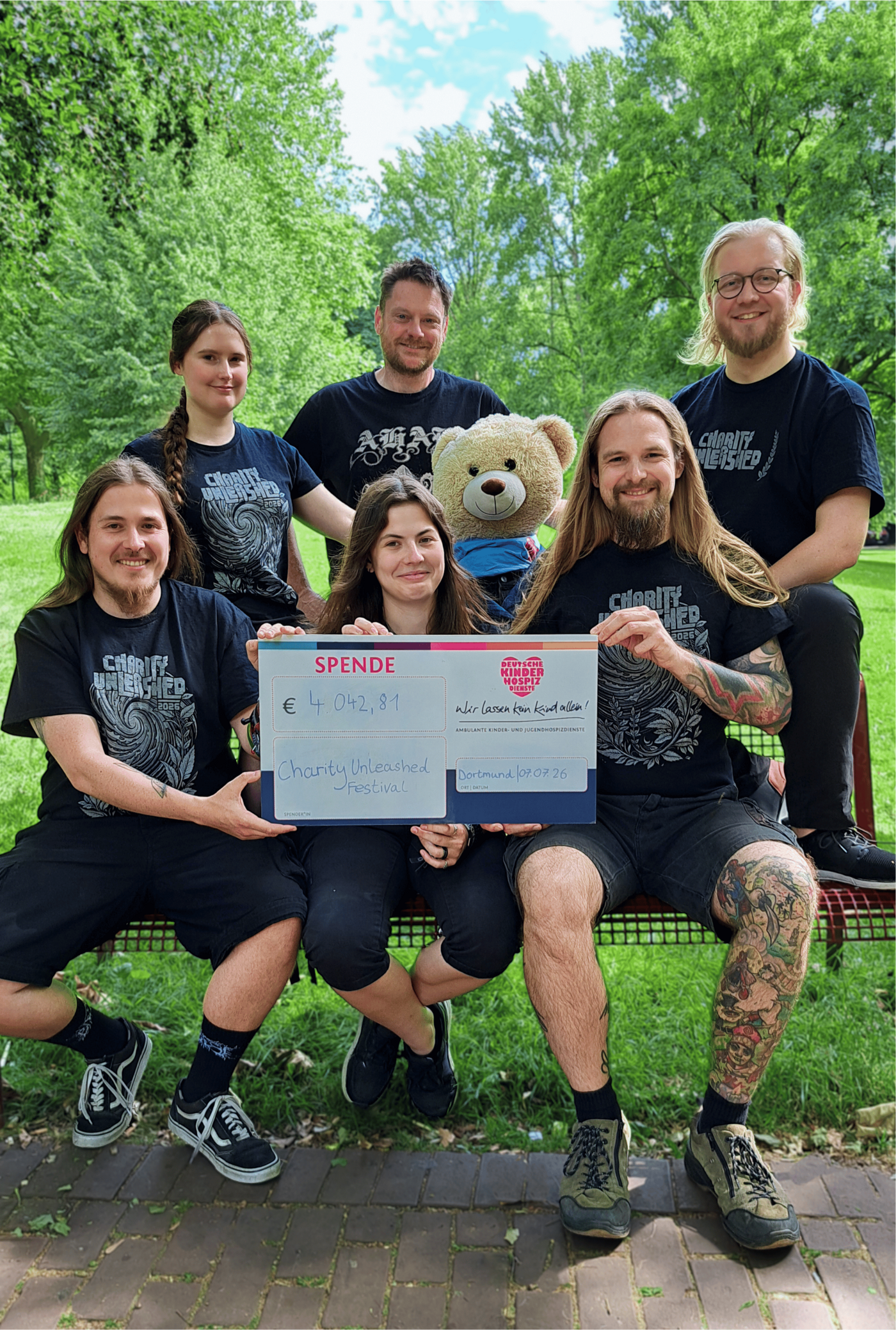 Freuen sich, dass das Spenden-Ergebnis vom Vorjahr erneut getoppt werden konnte: In Dortmund  überreichten Joël Pakulat, Michelle Reinecke, Dominik Kytzia (sitzend von links) und Nena S. (stehend  links) den symbolischen Spendenscheck vom „Charity Unleashed“-Festival an Thomas Ballhoff  (hinten Mitte), Michael Cremann (hinten rechts) sowie Bärenbotschafter Hope von den Deutschen  Kinderhospiz Diensten.  (Quelle: Deutsche Kinderhospiz Dienste / Simke Strobler)